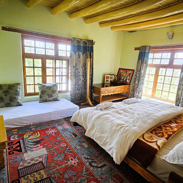 Homestay bedroom with wooden ceiling, large windows and a Tibetan carpet